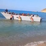 Staggering moment beachgoers push packed migrant boat BACK off Greek tourist beach after they sailed across from Libya