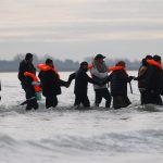 Migrants join hands making way to small boat which eventually collapsed in the Channel en route to UK